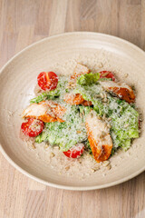 Fresh salad with roasted chicken, cherry tomatoes, and cheese in a rustic bowl on wooden table