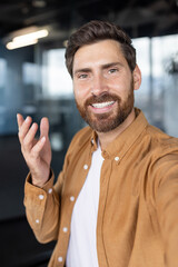 A man smiles during a video call, wearing a casual shirt and expressing himself with gestures