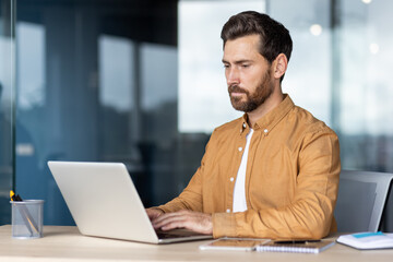 A focused businessman working on a laptop in an office environment, showcasing concentration and...