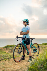 Obraz premium vertical Latin cyclist woman standing with her gravel bike in front of the sea at sunrise