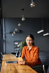 Young Indian business woman manager ceo using cell phone mobile app laptop. Smiling Latin Hispanic mature female businesswoman holding smartphone in office trading, reading, working online. Vertical