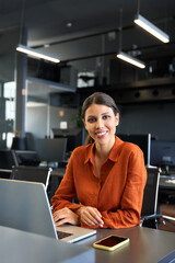 European mature manager woman using computer for finance analysing work online. Financial specialist latin hispanic businesswoman working on laptop pc sitting in office. Vertical portrait at camera