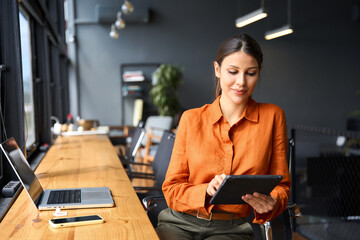 Successful smiling latin hispanic young woman using pad computer for business app. Busy executive CEO businesswoman professional holding digital tablet pc device for work in modern office workplace. 