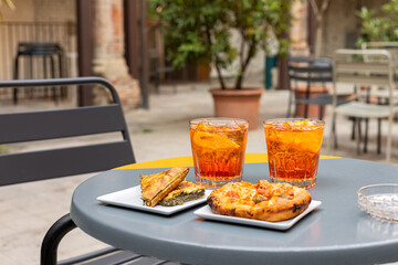 Glasses with Aperol Spritz, pre-dinner drinks, and complimentary italian snacks on a table in...