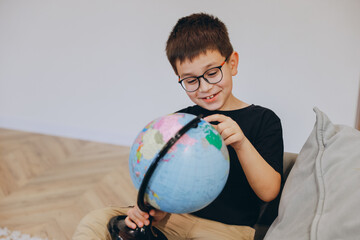 Curious boy exploring world geography with rotating globe at home