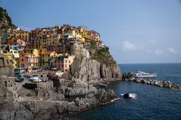 Colorful cliffside houses of Manarola village with rocky beach and turquoise sea, Cinque Terre, Italy - Picturesque coastal town on the Italian Riviera (182 characters)