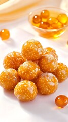 A close-up shot of a pyramid of small, golden-brown, textured spheres, possibly confectionery, sits on a white surface.  A small glass bowl of similar spheres is visible in the background, along