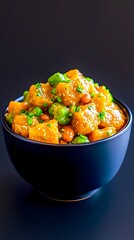 A dark-blue bowl brimming with a vibrant mix of cubed butternut squash, edamame, and peas, glistening with a light sauce and garnished with finely chopped scallions, sits against a stark black