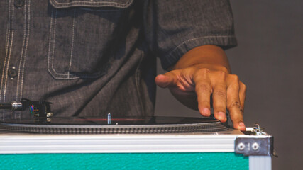 DJ man wearing black shirt is playing a vinyl disc record on disc player. The DJ playing music by using his finger to Scratching the disc during live performer for audience.