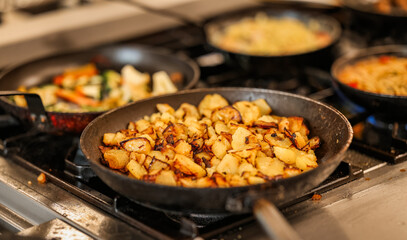 Close-up of golden roasted potatoes frying in a pan on a gas stove, surrounded by other sizzling...