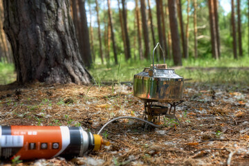 A stainless steel kettle stands on a gas burner in the forest at a picnic. Summer picnic in a pine forest.