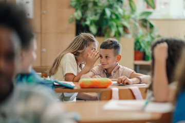 Girl whispering secret to a classmate during class at elementary school