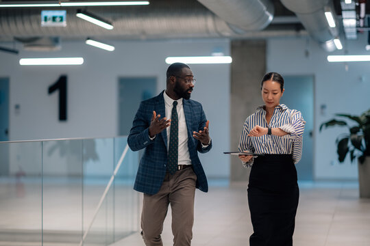 Businesspeople discussing while walking in office corridor and checking time