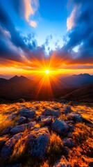 Vibrant sunset over a mountainous landscape, with the sun's rays bursting through clouds, casting a warm glow on rocky terrain and sparse vegetation in the foreground