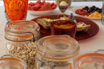 Glass jars with various cereals on a table set for breakfast