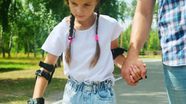 Father and daughter ride on roller skates. Girl learning to roller skate. Dad teaches daughter to ride on rollers