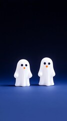 Two small, white ghost figurines stand on a dark blue surface against a matching backdrop.  They have simple orange mouths and small blue eyes