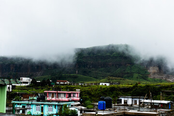 Hillside town shrouded in mist, with colorful houses and lush green mountains in Meghalaya. 