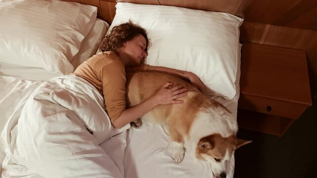 Woman sleeping peacefully with her corgi dog in cozy bed