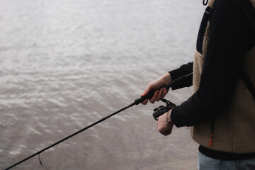 Side view of a man holding a spinning rod while fishing at a calm lake, dressed in casual outdoor...