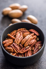 Peeled pecan nuts in bowl on black table.