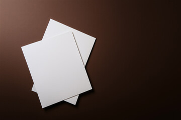 Blank sheets rest elegantly on a rich brown surface in warm light
