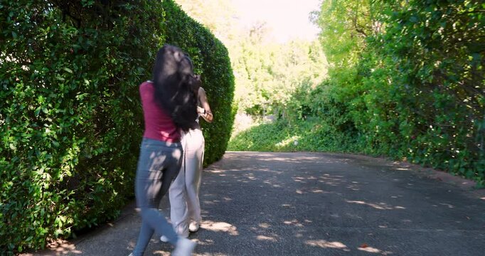 Diverse female friends walking garden path stopping and taking selfie, sharing smartphone images