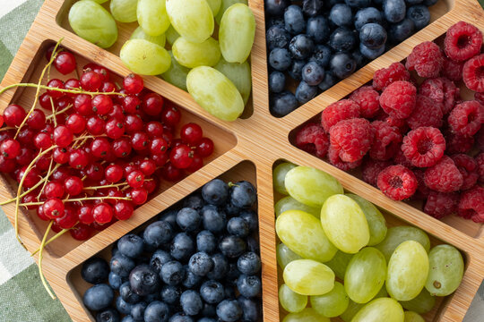 Top view of colorful fresh berries and grapes served in wooden tray on table. Concept of healthy eating, organic food, summer fruit variety and balanced nutrition for active lifestyle
