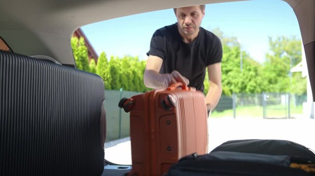 Man loading suitcases, bag and backpack into car trunk near suburban house. Preparing for travel by packing luggage into vehicle. Concept of relocation or road trip