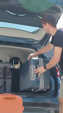 Man loading suitcases into car trunk near suburban house. Preparing for travel by packing luggage into vehicle. Concept of relocation or road trip