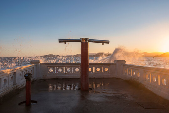 Santos city, Brazil. Waves crashing against the beach wall near the shower. Sunset in Santos Bay. Ponta da Praia District.