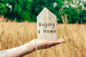 Person is holding a wooden sign that says buying a home