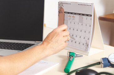 Close up of the hand of a female doctor pointing a calendar on the desk and medical instruments.