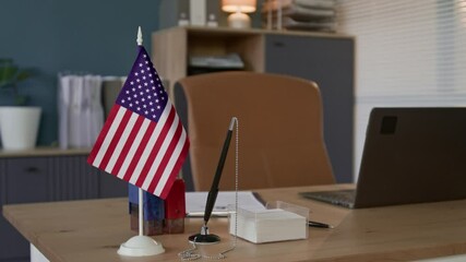 Selective focus shot of US flag next to pen, small box with post-it notes, two stamps, clipboard and laptop at workplace of visa processing officer - Powered by Adobe