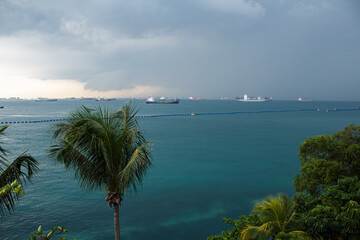 Ominous storm clouds gather over a busy ocean, with numerous cargo ships dotting the horizon. Palm...