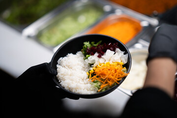 Hand holding a black bowl filled with rice and colorful shredded vegetables.