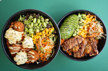 Two poke bowls with falafel, avocado, grilled meat, and vegetables, top view, isolated on green background.
