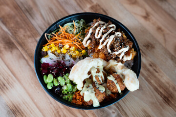 Poke bowl with vegetables, rice, and crispy toppings, top view, isolated on wooden background.