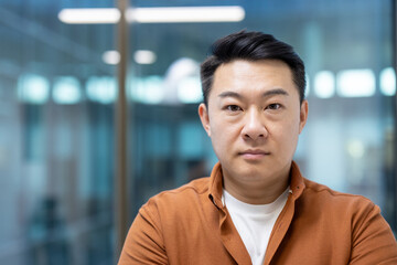Obraz premium A portrait of an Asian man looking directly at the camera with a serious expression. He is wearing a brown shirt.