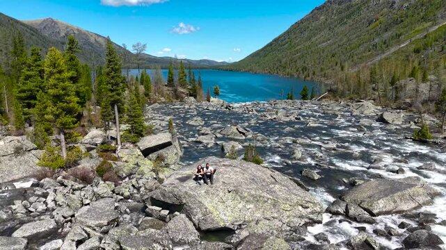 A couple travels through Altai. A couple takes a selfie while climbing the mountain Multinsky lakes. Hiking, backpacking, tourists on the rocks of a mountain lake, drone view