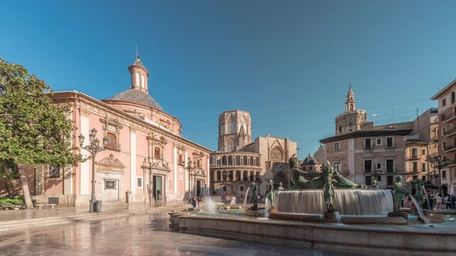 Panorama showing timelapse of Valencia's Plaza de la Virgen, showcasing Turia Fountain, Cathedral and Basilica de la Virgen de los Desamparados in Spain's historic old town under a blue sky