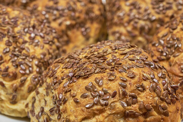 Whole grain concept. Homemade baked whole wheat rolls decorated with flaxseeds, close-up photo