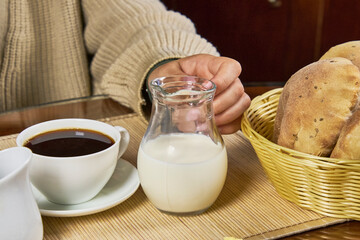 Close-up of a woman eating a healthy breakfast in the kitchen with bread, coffee, milk, jam, butter, and cheese.