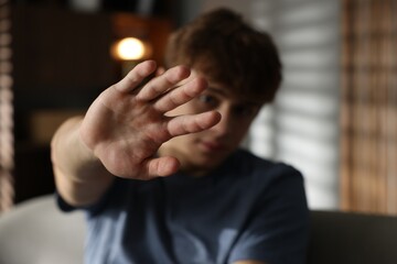 Teen problems. Upset teenage boy making stop gesture at home, selective focus