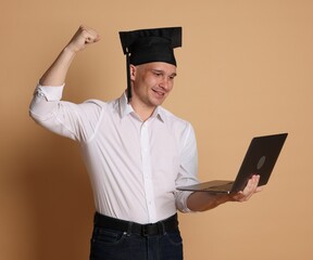 Happy student with laptop after graduation on beige background