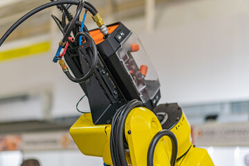 Large yellow industrial robot with complex joints and cables, positioned on an industrial floor or manufacturing plant setting Artificial diffused lighting, no people or animals present, perspective