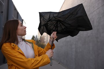 Teenage girl with broken umbrella fighting wind under rain outdoors