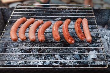 Person grilling vegetables, sausages, chicken, trout over charcoal in a backyard during summer. Outdoor cooking with real flames and smoke in a cozy home setting
