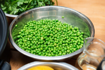 Fresh green peas in metal bowl on counter. Close-up of vibrant green peas in a stainless steel...