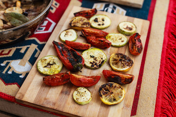 Person grilling vegetables, sausages, chicken, trout over charcoal in a backyard during summer. Outdoor cooking with real flames and smoke in a cozy home setting